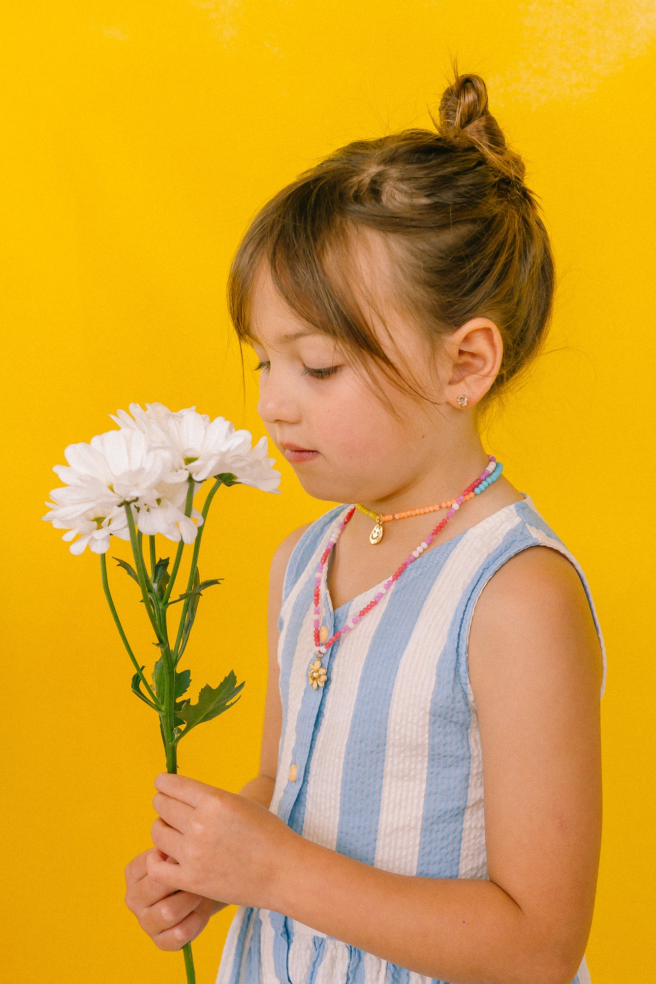 Girl in a light blue dress wearing the handmade Daisy Necklace with golden pendant and pink crystal chain.