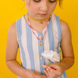Girl in a blue dress looking down while wearing the handmade Daisy Necklace with golden pendant.