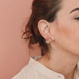 Profile of a woman wearing a Galaxea earring in Rust color, gold-plated with glass granules, hair pulled back, against a soft terracotta background.