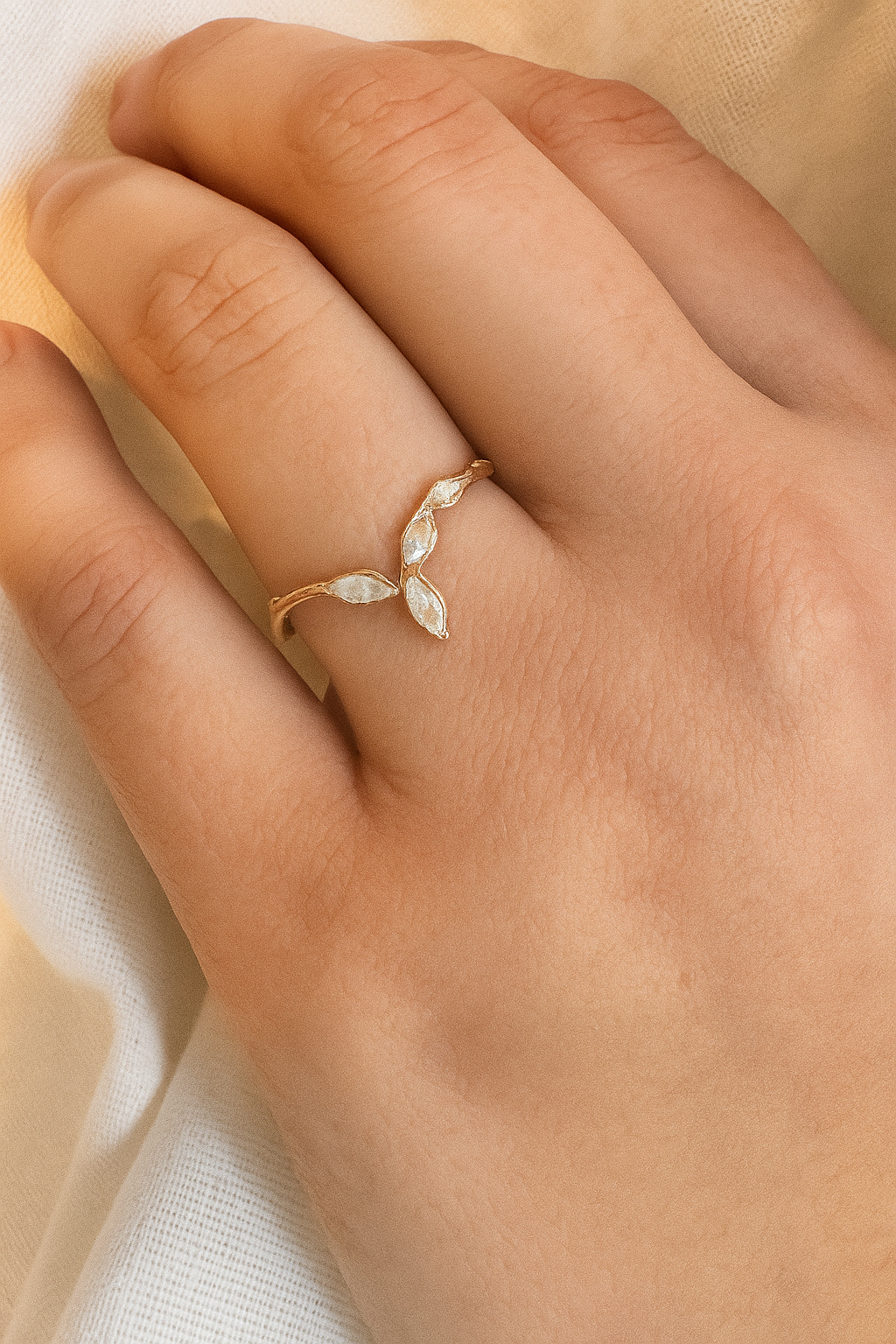 Rose gold Marqueza ring with zircons worn on a hand, photographed over soft fabric.