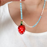 Close‑up torso shot of a child wearing a white sleeveless top and the Strawberry Necklace, with the red strawberry pendant centered.