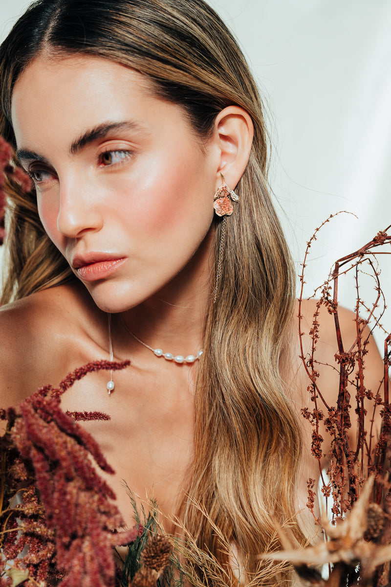 Red elderberry earrings in gold-plated brass with coral granulation, worn by model among dry foliage, in close-up shot of face.