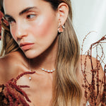 Red elderberry earrings in gold-plated brass with coral granulation, worn by model among dry foliage, in close-up shot of face.