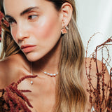 Red elderberry earrings in gold-plated brass with coral granulation, worn by model among dry foliage, in close-up shot of face.