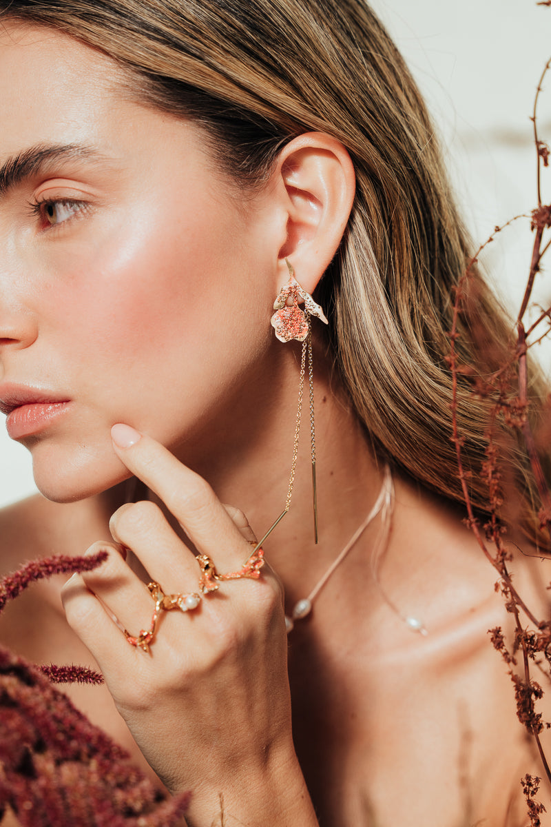 Red elderberry earrings in gold-plated brass with coral granulation, worn by model among dry foliage, in close-up shot of face.