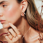 Red elderberry earrings in gold-plated brass with coral granulation, worn by model among dry foliage, in close-up shot of face.