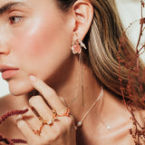 Red elderberry earrings in gold-plated brass with coral granulation, worn by model among dry foliage, in close-up shot of face.