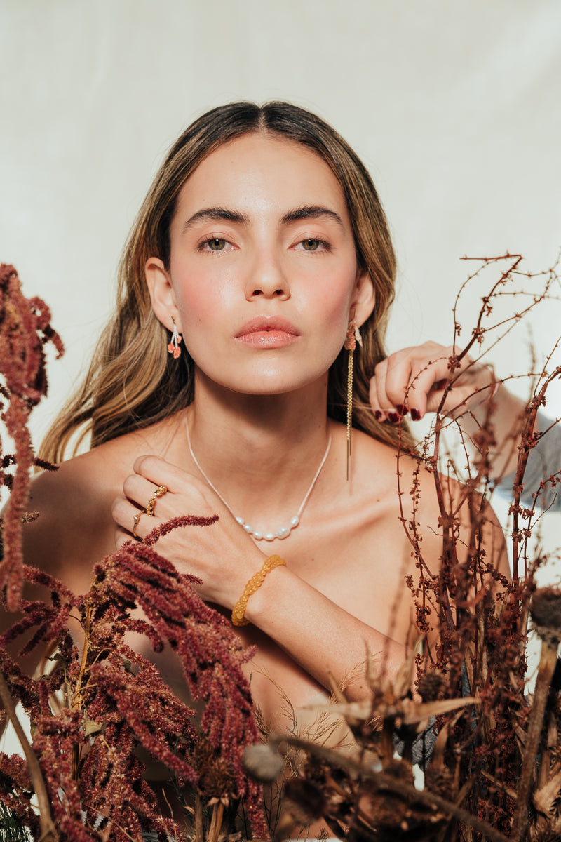 Red elderberry earrings in gold-plated brass with botanical texture, worn by a model with a light background and plant composition.