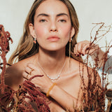 Red elderberry earrings in gold-plated brass with botanical texture, worn by a model with a light background and plant composition.