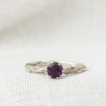 Close-up of a sterling silver ring featuring a 4mm round amethyst set in a textured band, displayed on soft white fabric.