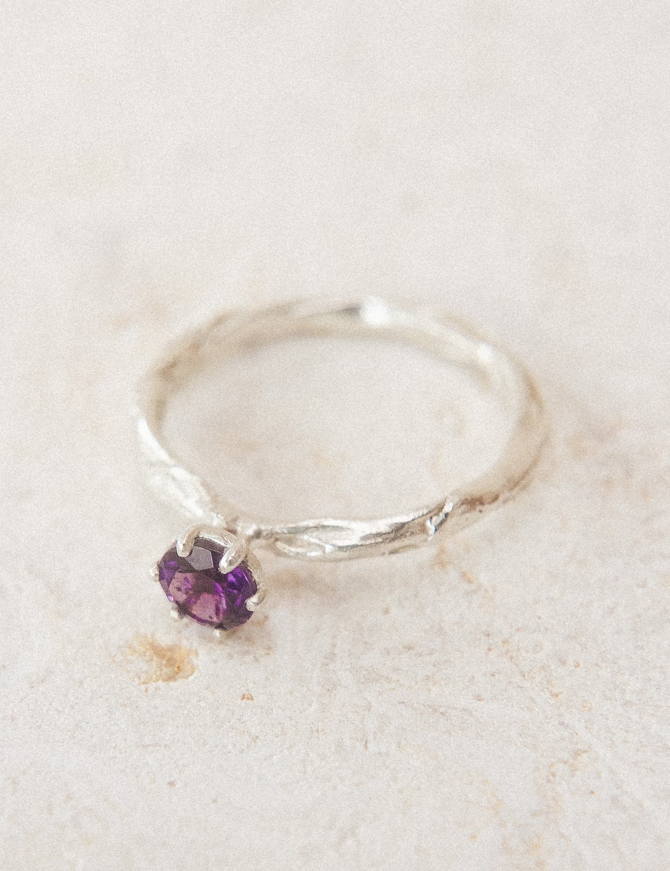 Top view of the sterling silver ring with a 4mm amethyst, placed on neutral fabric, highlighting its organic handcrafted texture.
