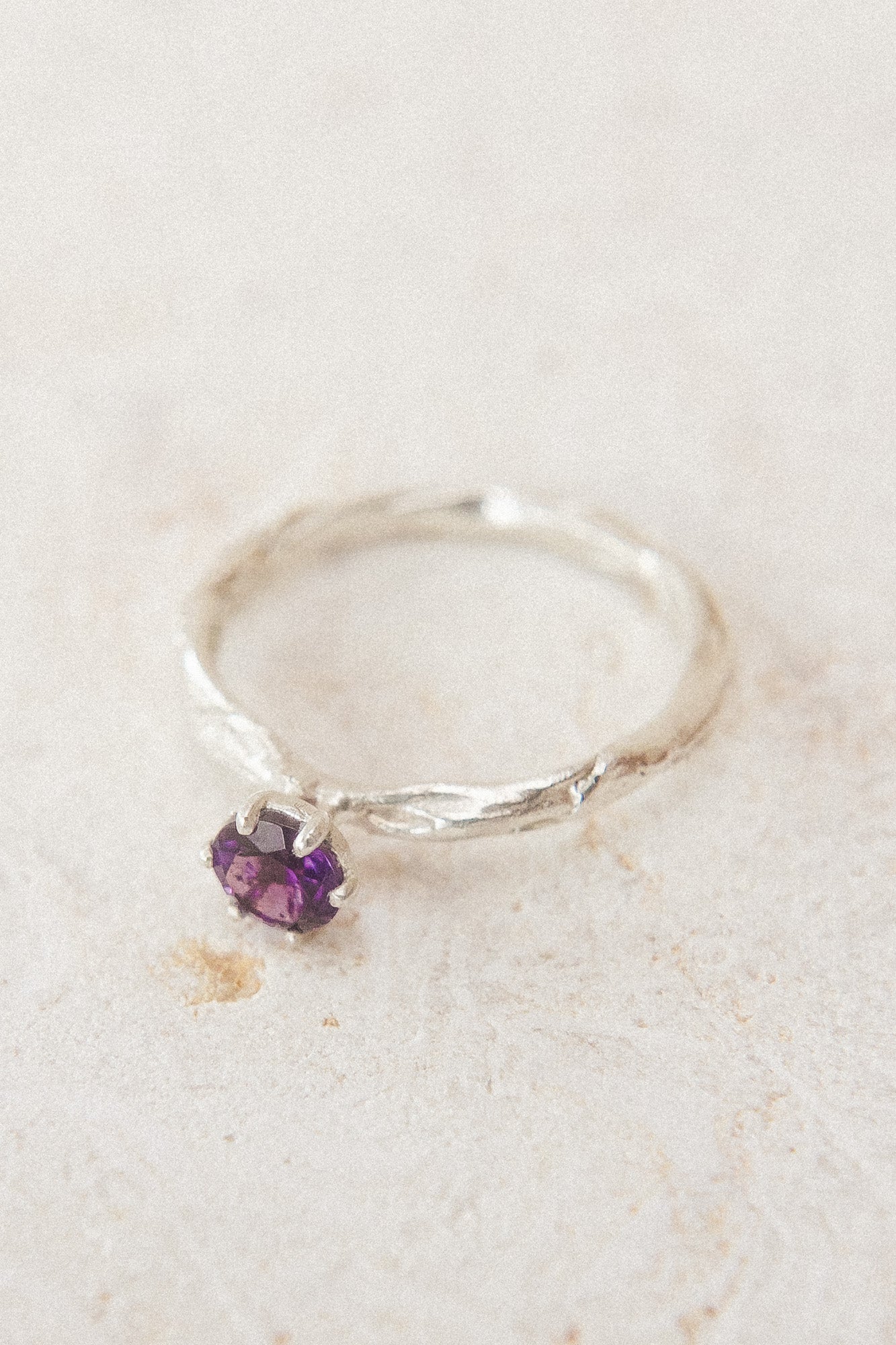 Top view of the sterling silver ring with a 4mm amethyst, placed on neutral fabric, highlighting its organic handcrafted texture.