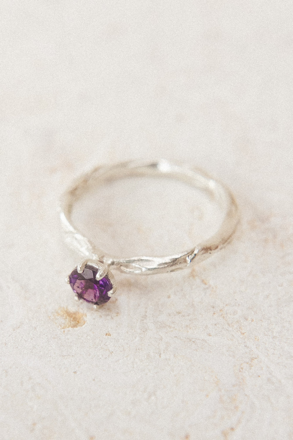Top view of the sterling silver ring with a 4mm amethyst, placed on neutral fabric, highlighting its organic handcrafted texture.