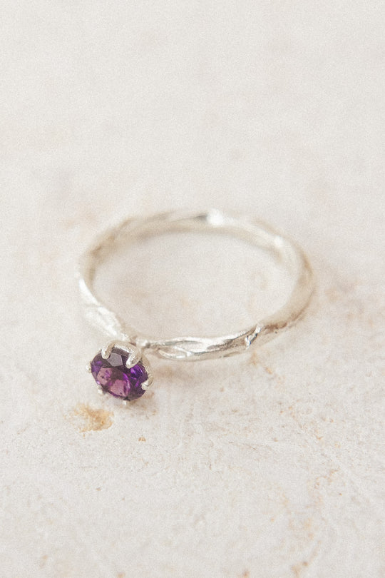 Top view of the sterling silver ring with a 4mm amethyst, placed on neutral fabric, highlighting its organic handcrafted texture.