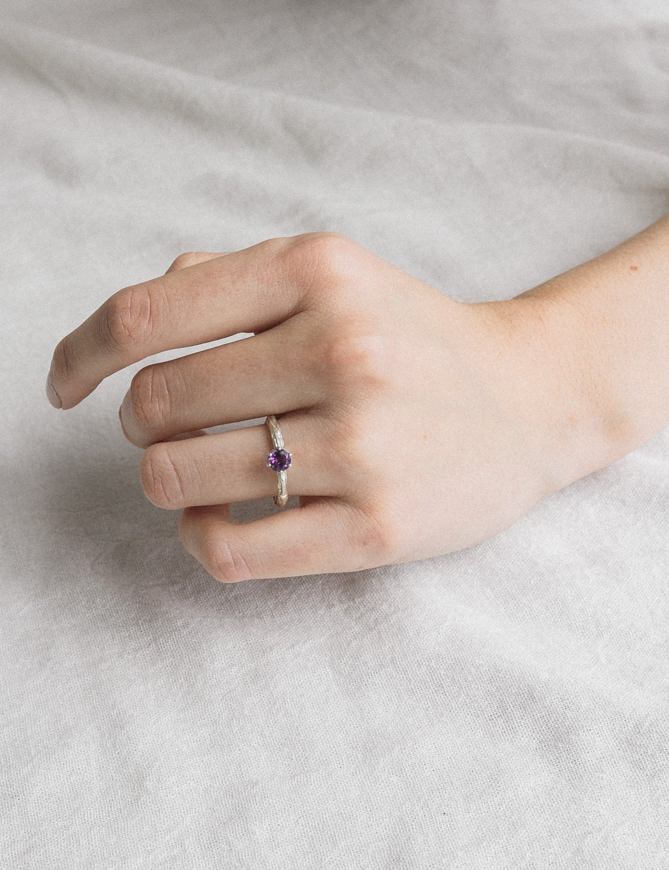 Woman’s hand wearing the sterling silver amethyst ring, showing the fit and delicate profile of the 4mm gemstone against a soft background.