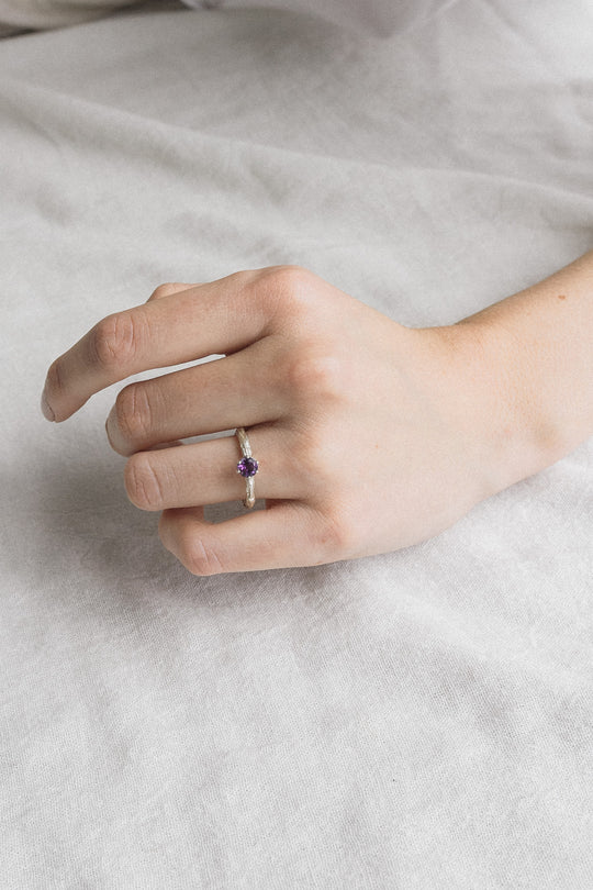 Woman’s hand wearing the sterling silver amethyst ring, showing the fit and delicate profile of the 4mm gemstone against a soft background.