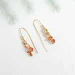Azahar Earrings in red tones on a light background with blurred botanical-style branches.