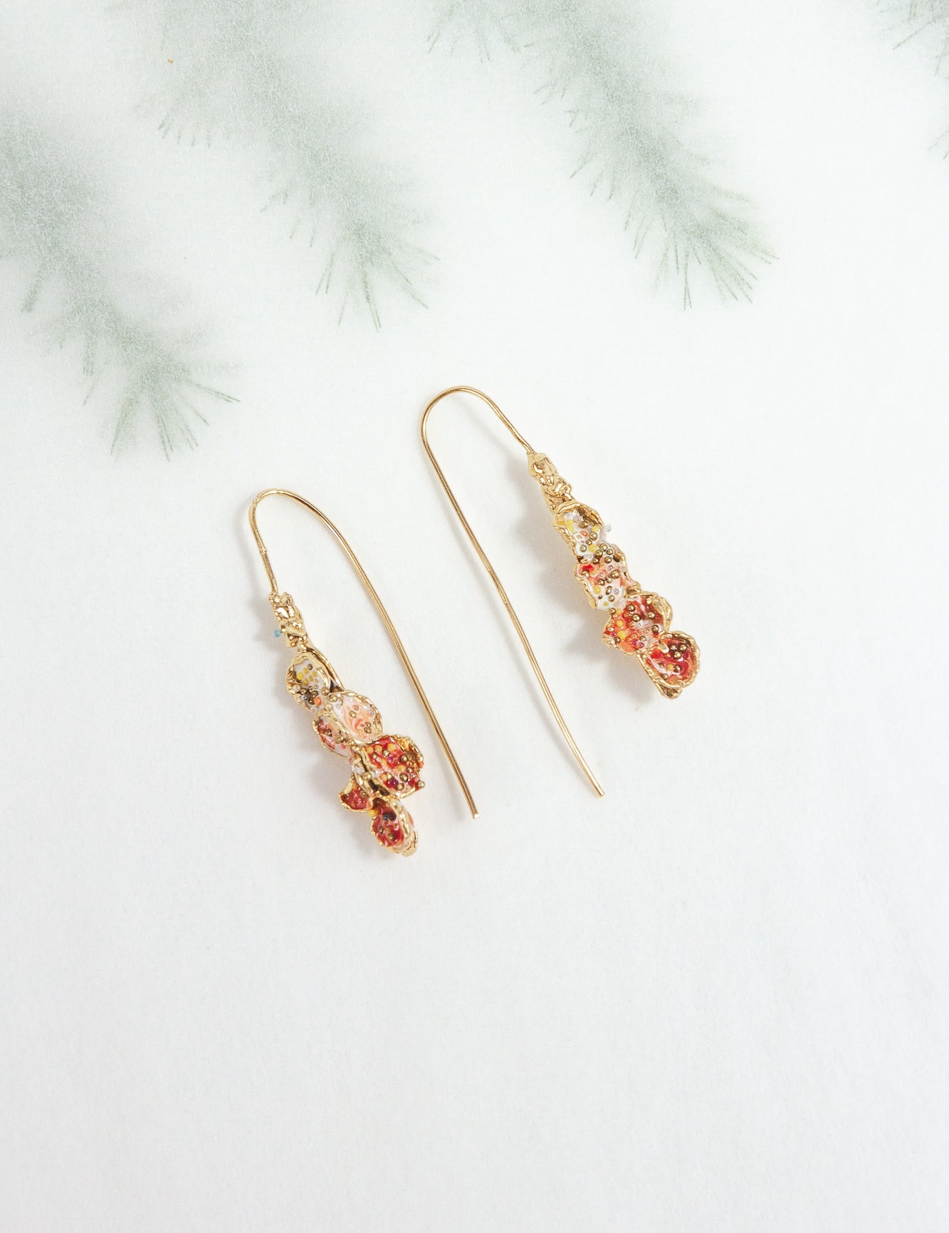 Azahar Earrings in red tones on a light background with blurred botanical-style branches.