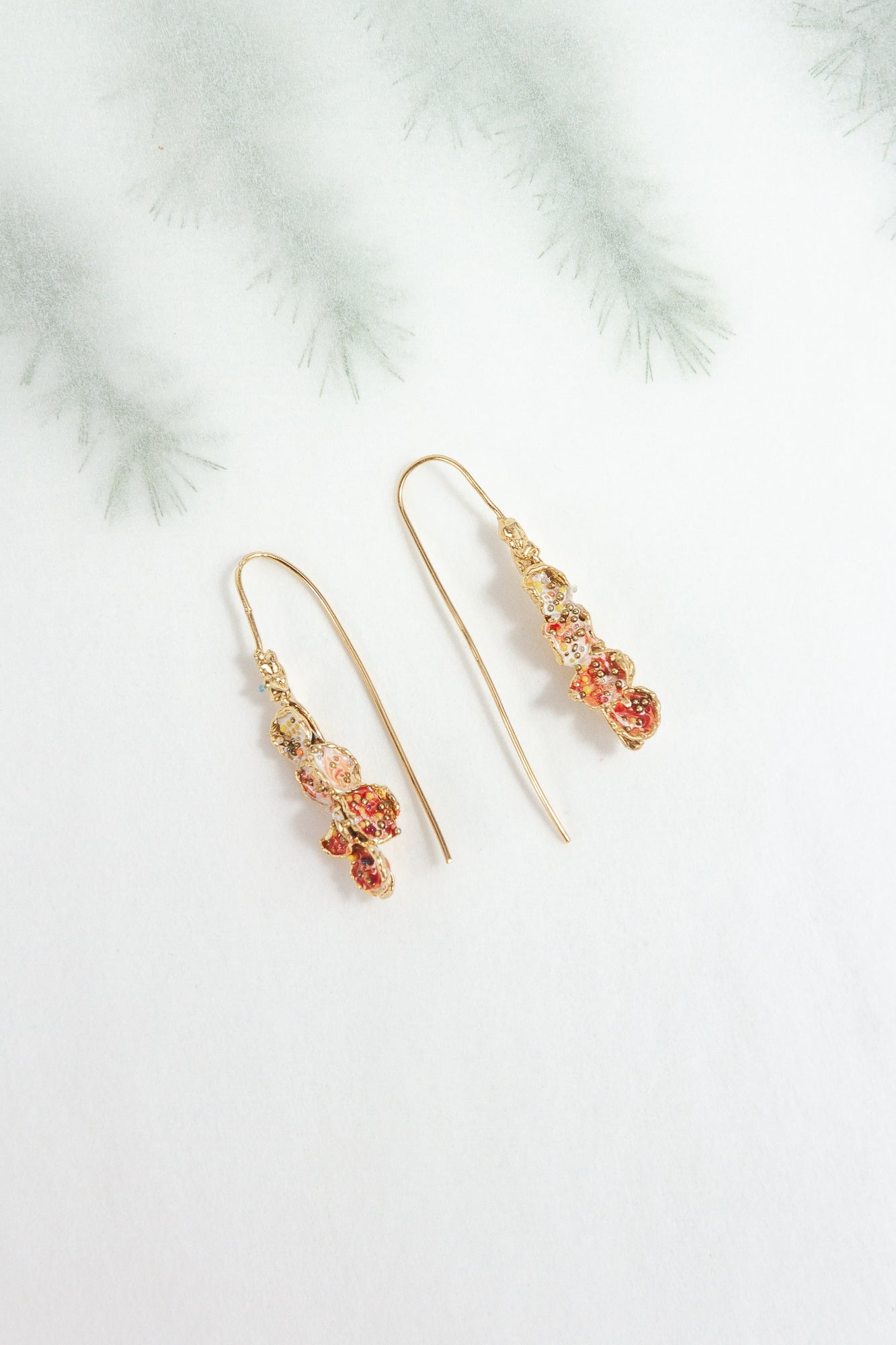 Azahar Earrings in red tones on a light background with blurred botanical-style branches.