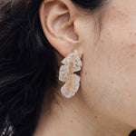 “Close-up side view of a woman’s ear wearing a single Banana Leaf Earring painted in sage-green with glass granulation on a gold-plated bronze setting, hair tucked behind ear against a neutral background.