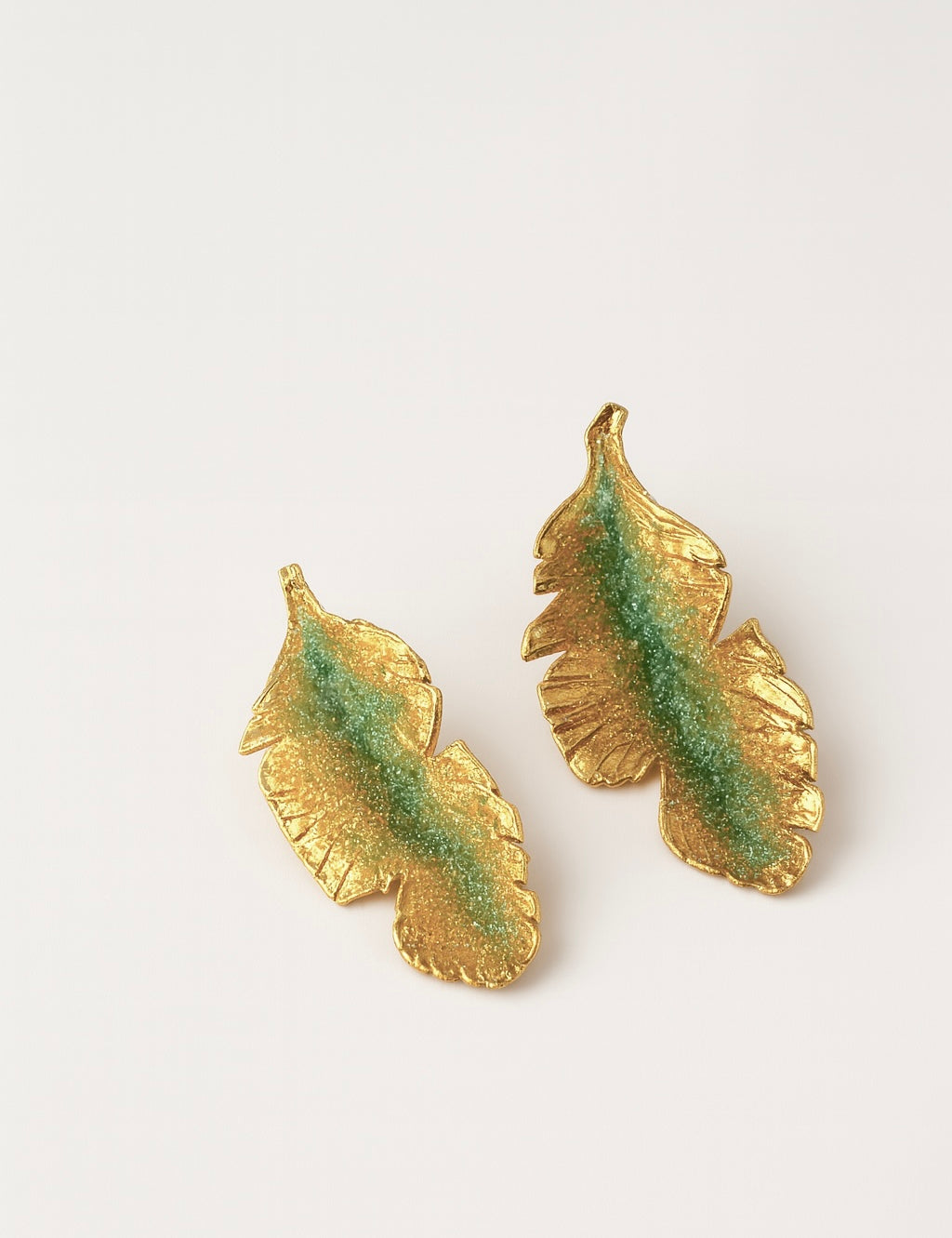 Pair of Banana Leaf Earrings in gold-plated brass hand-painted sage-green with glass granulation detail, displayed against a white background.