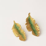 Pair of Banana Leaf Earrings in gold-plated brass hand-painted sage-green with glass granulation detail, displayed against a white background.