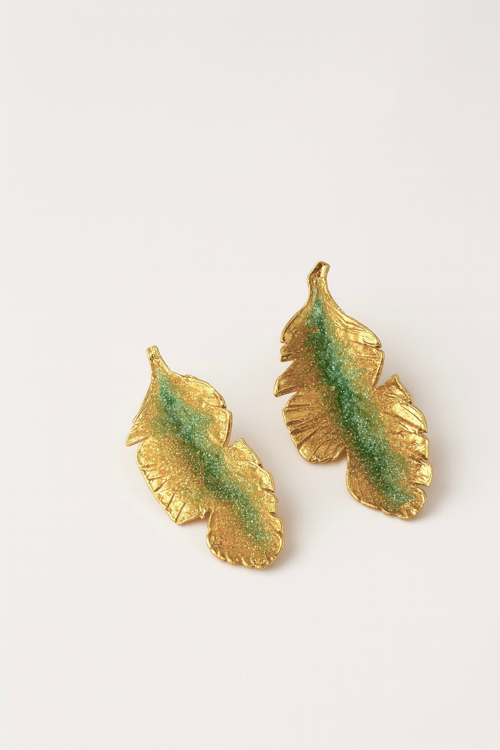 Pair of Banana Leaf Earrings in gold-plated brass hand-painted sage-green with glass granulation detail, displayed against a white background.