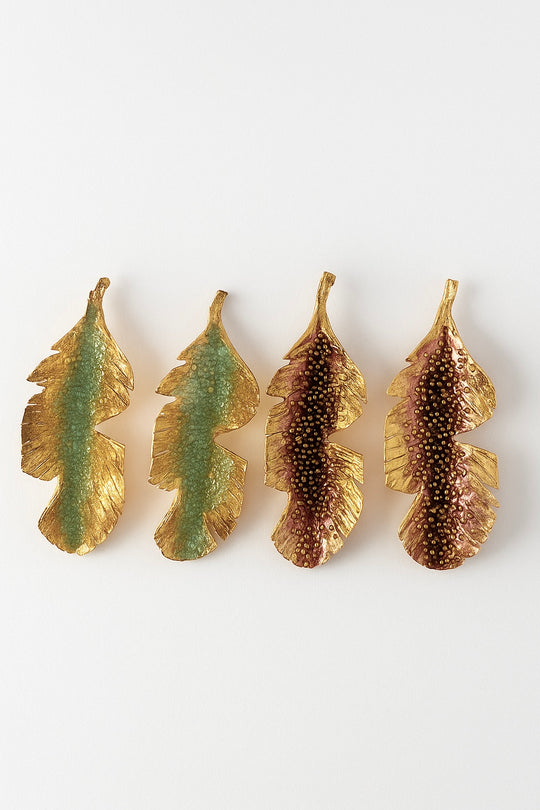 Flat lay of four Banana Leaf Earrings arranged horizontally on a white background—two hand-painted in sage-green and two in rust—with glass granulation and gold-plated bronze settings.