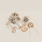 Flat lay of ocean-inspired jewelry, including gold-dipped shells, pearl and gemstone necklaces, earrings, and hairpins, displayed on a white textured surface.