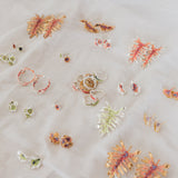 Colorful assortment of handcrafted rings and earrings inspired by nature, featuring floral and coral-like designs in gold, silver, and vibrant resins, displayed on a soft white fabric.
