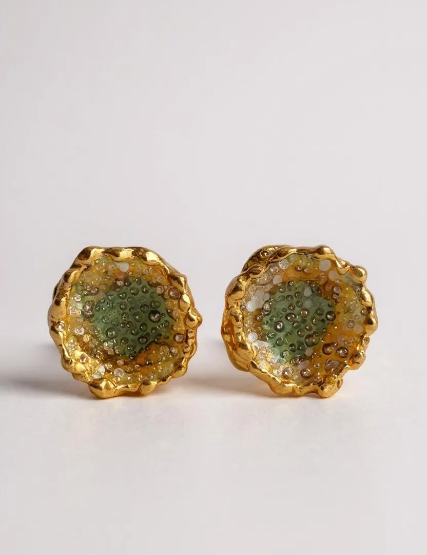 Flat lay of a pair of Topos Coca M stud earrings in gold-plated brass, hand-painted in sage-green with glass granulation, on a white background.