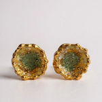 Flat lay of a pair of Topos Coca M stud earrings in gold-plated brass, hand-painted in sage-green with glass granulation, on a white background.