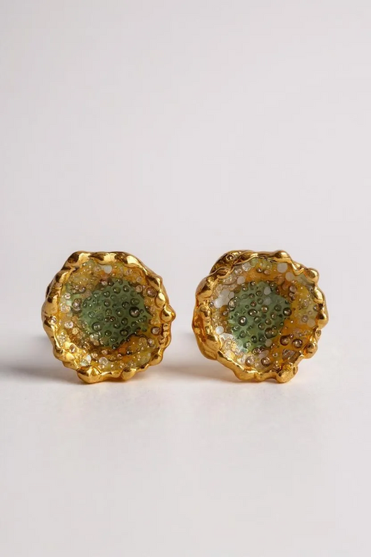 Flat lay of a pair of Topos Coca M stud earrings in gold-plated brass, hand-painted in sage-green with glass granulation, on a white background.