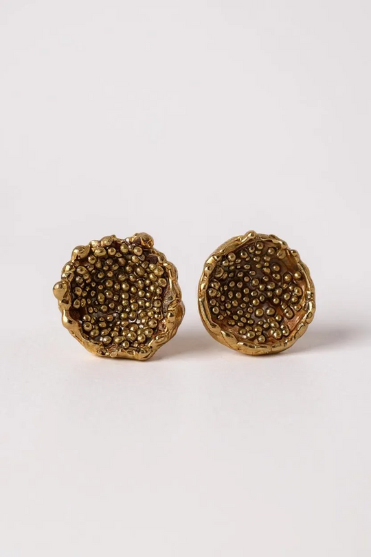 “Flat lay of a pair of Topos Coca M stud earrings in gold-plated bronze, hand-painted in rust with glass granulation, on a white background.