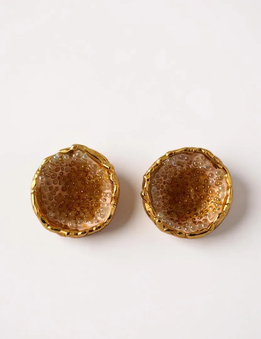 Flat lay of a pair of Topos Coca M stud earrings in gold-plated brass, hand-painted in sunset with turquoise glass granulation, on a white background.