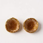 Flat lay of a pair of Topos Coca M stud earrings in gold-plated brass, hand-painted in sunset with turquoise glass granulation, on a white background.