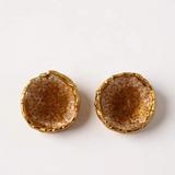 Flat lay of a pair of Topos Coca M stud earrings in gold-plated brass, hand-painted in sunset with turquoise glass granulation, on a white background.