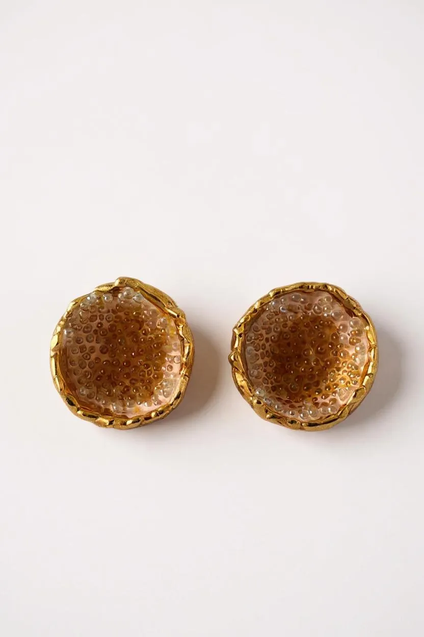 Flat lay of a pair of Topos Coca M stud earrings in gold-plated brass, hand-painted in sunset with turquoise glass granulation, on a white background.