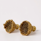 Close-up of two Topos Coca M stud earrings in gold-plated bronze featuring detailed glass granulation texture, displayed on a pale neutral background.