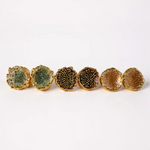 Flat lay of six Topos Coca M stud earrings on a white background, showing all three hand-painted variants—two in sage-green with glass granulation, two in rust with glass granulation, and two in sunset paint with turquoise granulation—each set in gold-plated bronze.