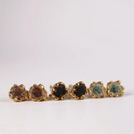 Six Topos Coca S stud earrings arranged in a horizontal line on a pale background, each featuring a scalloped gold-tone setting filled with glass granulation and painted finishes in shades of brown, black, green, turquoise, and more
