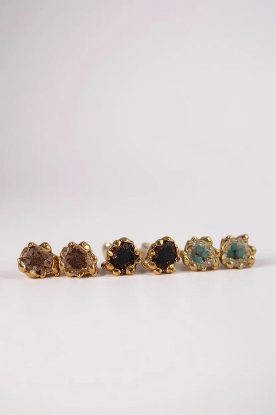 Six Topos Coca S stud earrings arranged in a horizontal line on a pale background, each featuring a scalloped gold-tone setting filled with glass granulation and painted finishes in shades of brown, black, green, turquoise, and more