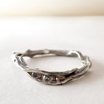 Handcrafted silver ring with lab-grown diamonds, organic branch-like design, placed on a white surface.
