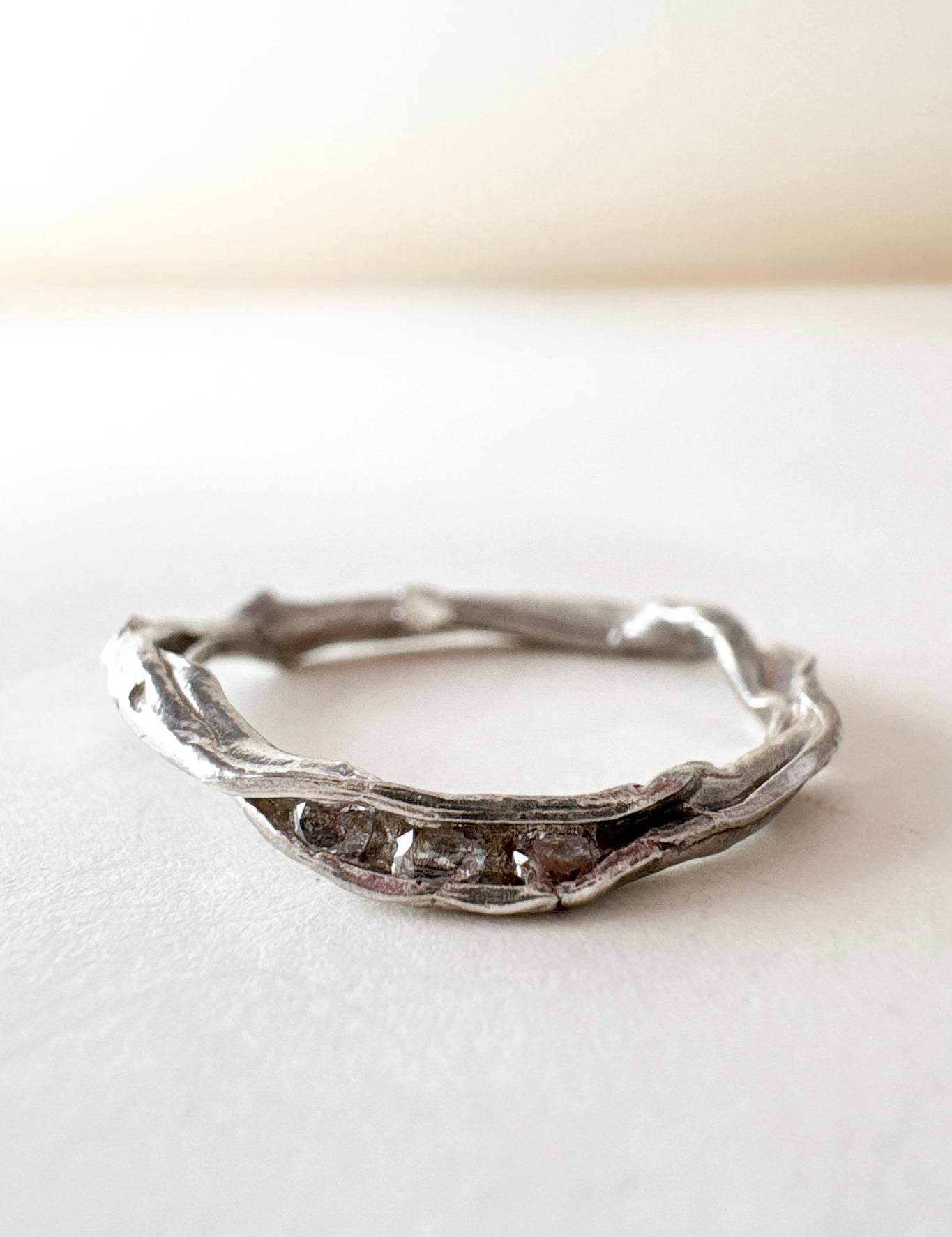 Handcrafted silver ring with lab-grown diamonds, organic branch-like design, placed on a white surface.