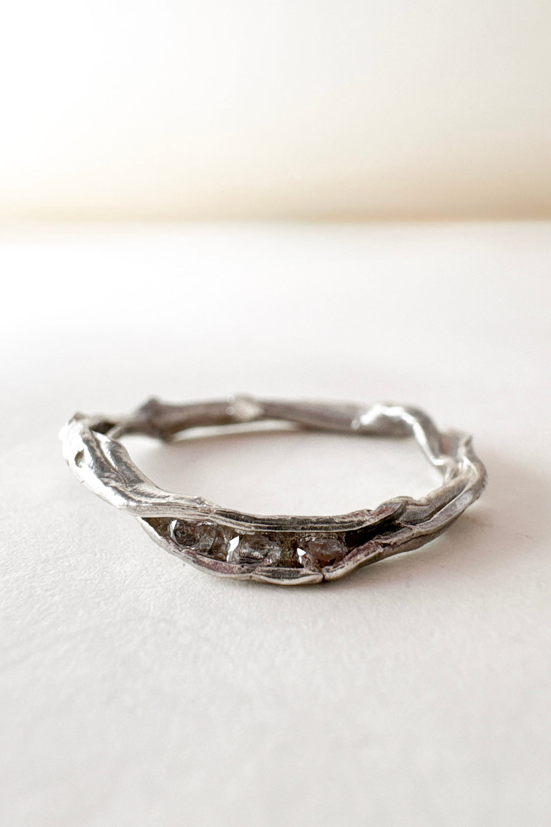 Handcrafted silver ring with lab-grown diamonds, organic branch-like design, placed on a white surface.