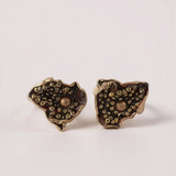 “Pair of Topos Cucu stud earrings in rust paint with glass granulation on gold-plated bronze, displayed on a soft pink background.