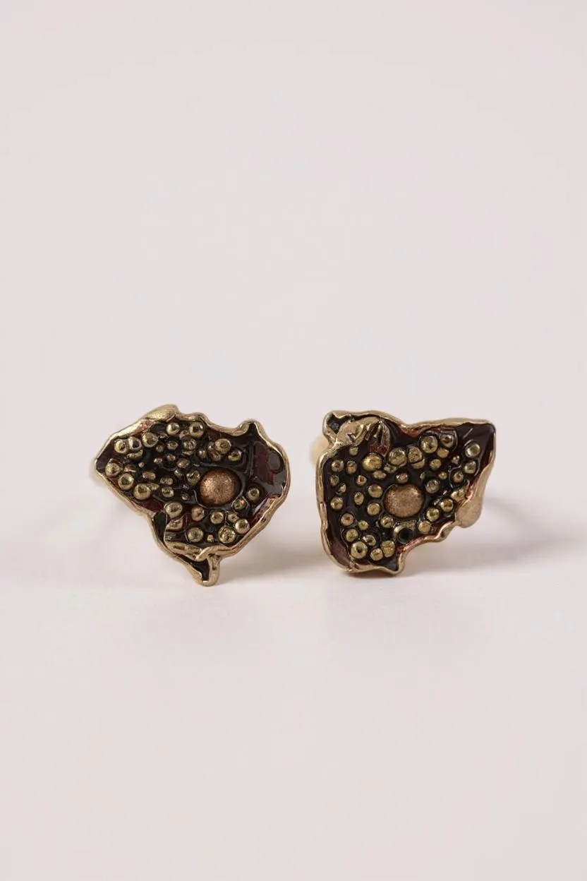 “Pair of Topos Cucu stud earrings in rust paint with glass granulation on gold-plated bronze, displayed on a soft pink background.