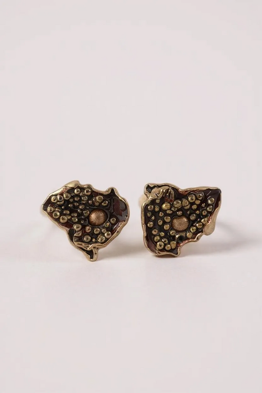 “Pair of Topos Cucu stud earrings in rust paint with glass granulation on gold-plated bronze, displayed on a soft pink background.