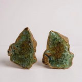 Flat lay of two Topos Cucu stud earrings hand-painted in sage-green paint with glass granulation on gold-plated brass, displayed on a white background.