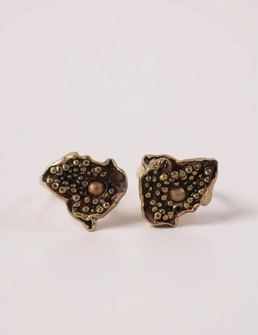 “Pair of Topos Cucu stud earrings in rust paint with glass granulation on gold-plated bronze, displayed on a soft pink background.